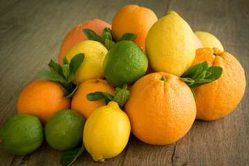 Closeup view of colorful pile of ripe citrus fruits and leaves of mint on wooden table. Solid juicy orange, grapefruit, lemon, lime, tangerine lying on brown surface. Summertime harvesting
