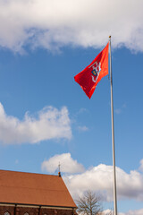 Vertical photo of historical Lithuanian flag with Vytautas the great figure and a metal cross at the stone cathedral roof against sky background. Flag with an armour-clad knight on horseback