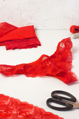 Red lace lingerie, female panties, tailor workplace equipment fabric, scissors, thread. Handmade underwear workshop