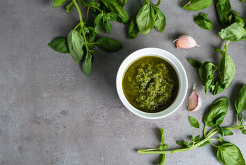 Obraz na płótnie Canvas Pesto sauce. Pesto in a bowl, fresh basil and garlic on a gray background. View from above
