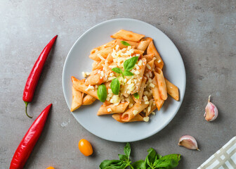 Pasta penne alla arrabiata with basil and cheese on gray background. Classic italian pasta penne with chili sauce arrabbiata.