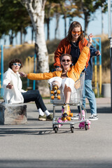 laughing woman in roller skates riding in shopping cart near happy multiethnic friends.