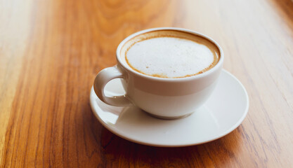 Cup of cappuccino coffee with a latte on a wooden bar in a sunlit cafe in the morning.