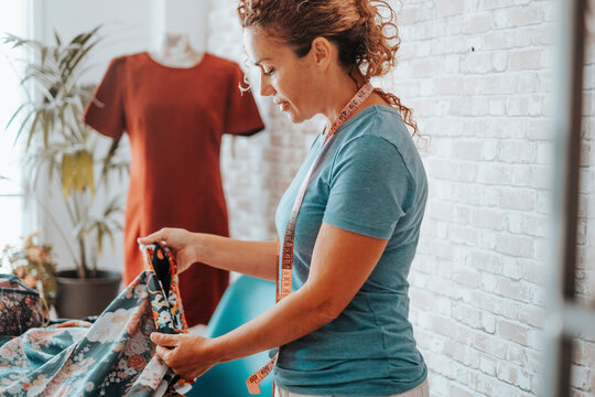 Woman in tailor activity at home or design studio store. Workshop of tailoring. Adule female working with textile and mannequin in background. Stylist lady creating clothes and enjoy hobby indoor