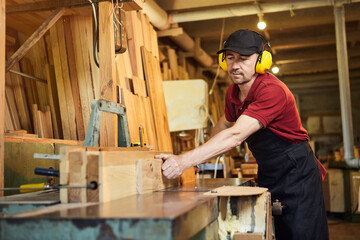 Senior carpenter in uniform works on a woodworking machine at the carpentry manufacturing