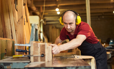 Senior carpenter in uniform works on a woodworking machine at the carpentry manufacturing