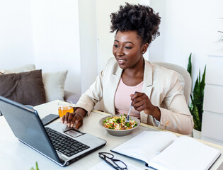African American young woman eating salad at the desk. Young woman working at home. Close up of a...