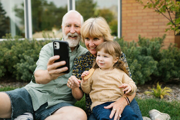 Smiling grandparents taking selfie with granddaughter (4-5) on back yard