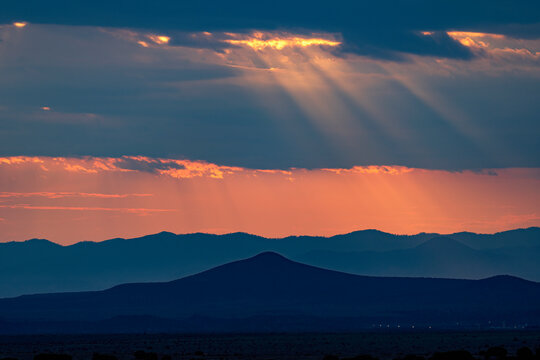 USA, New Mexico, Santa Fe, Sunbeams shining through storm clouds over mountains at sunset 