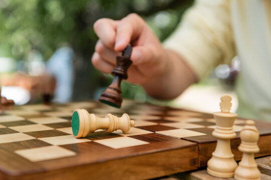 Cropped view of blurred man holding chess figure near board outdoors.