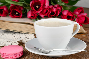 Cup of coffee, book, macaroon, tulips and knitted napkin on wooden table Closeup