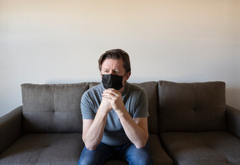 Pensive man in face mask sitting on sofa