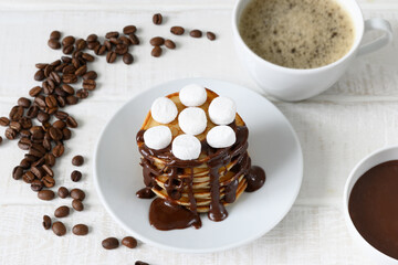Pancakes with chocolate syrup, cup of coffee and coffee beans on white table