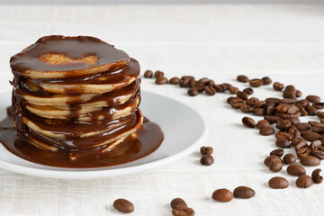 Pancakes with chocolate syrup on plate and coffee beans on white table