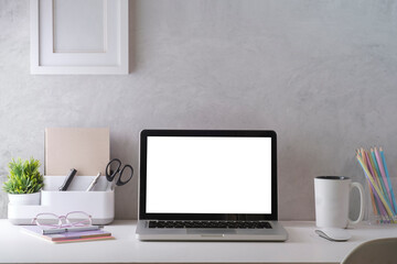 Mockup laptop with empty display, coffee cup, books and picture frame on white table.