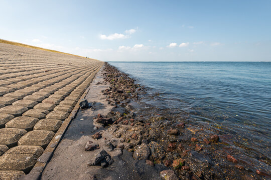 Dike revetment on the bank of a Dutch estuary. The photo was taken on the former island of Tholen in the province of Zeeland. Two cyclists are just visible at the end of the dike.