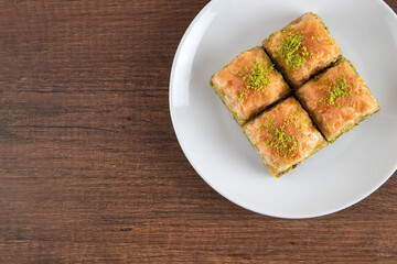 Pistachio baklava in a white plate on wooden background
