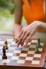 Cropped view of woman holding chess figure near board in park.