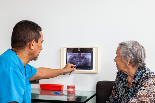 Male middle -aged dentist at his office using an x ray image to explain treatment to his senior woman patient