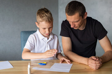 Naklejka premium A cute boy is sitting with his dad at the table and collecting origami. Adds up the details