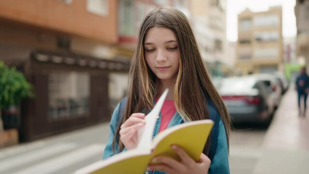 Adorable girl student reading book standing at street