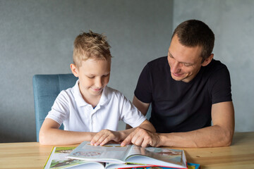 Naklejka premium A cute boy is sitting at the table with his dad and watching a book about butterflies