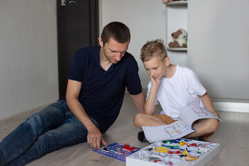 A cute boy in a white T-shirt collects an electrical designer with his dad in the room