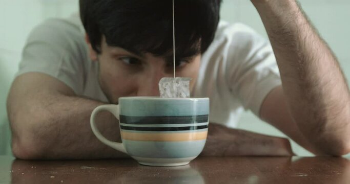 depression, problems-young alienated man plays with the tea bag staring at it