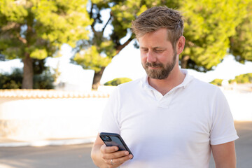 Close up portrait of a bearded man using his "smart phone", smiling outdoors.