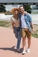 Positive couple hugging and holding longboard in park.