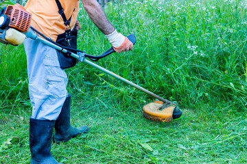 .A mature man in protective clothing, and gloves with a trimmer. .Mowing tall grass and the weeds with a trimmer. Selectively focus