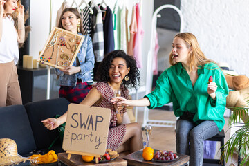 Young women at swap home party - clothes, shoes, bags, jewellery exchange between friends. Zero waste shopping, eco friendly concept, sustainable lifestyle. College life. 