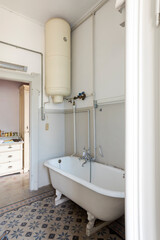Old bathroom with outdoor bathtub, exposed pipes, and black and white tiles