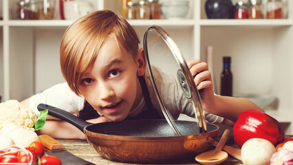 Child cooking. Cute little chef holding frying pan at kitchen. Funny boy wearing apron.