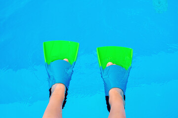 Kid legs with swim flippers over blue water background. Flippers in water. Diver fins. © volurol