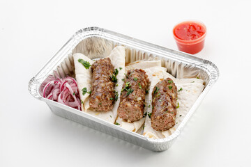 Pita with sausage on it with round onion, sauce, in the tray on a white background