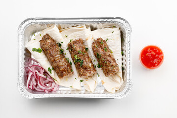 Pita with sausage on it with round onion, sauce, in the tray on a white background