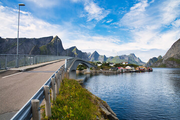 Fototapeta premium Single lane bridge connecting a small fishing village on Lofoten Islands, Norway. Dramatic mountain range next to the clear deep blue seawater. Wonderful vacation destination. 