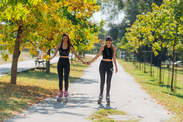 Obraz premium Beautiful sweet girlfriends riding on roller skates and holding hands on the street.