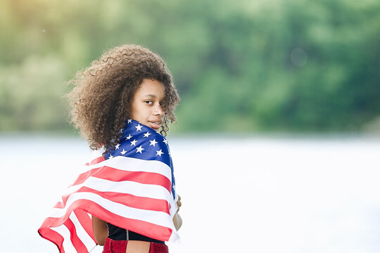 Young African american woman at nature background with an American USA flag on her shoulders. USA resident, US citizen. Immigration concept   