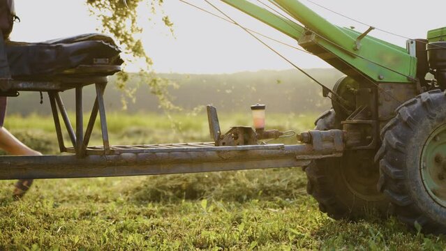 Motoblock - tillage equipment. In the background, a man gathers dry hay on the agricultural implement on fork and carries. A farmer collects dry grass to prepare food for cattle. Agriculture.