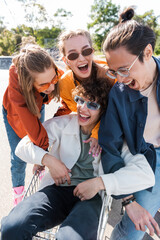multiethnic friends laughing near man sitting in shopping trolley.