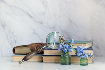 butterfly on blue flowers, magnifying glass and old books on table, abstract marble background....