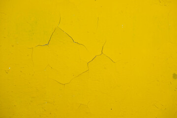 old wall painted with yellow paint with cracks and bubbles