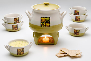 Ceramic soup kit with a pan, six bowls and a lit rechaud. One bowl has soup inside