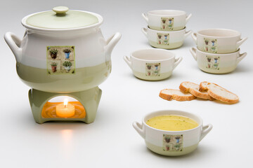 Ceramic soup kit with a pan, six bowls and a lit rechaud. One bowl has soup inside