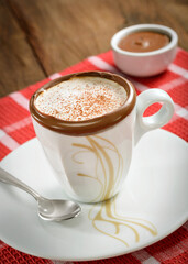Cup of cappuccino with chocolate on the edge, ambiented on a wooden table