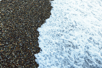 Seascape. Blue and gray pebbles on the beach. White sea waves. Skyline. Nature multicolored background.