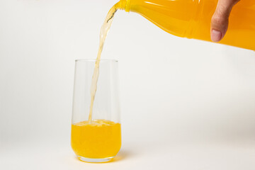 Glass of juice on a white background. Orange juice is poured into a glass from a bottle. Delicious and refreshing drink