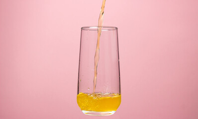 Glass of juice on a pink background. Orange juice is poured into a glass. Delicious and refreshing drink